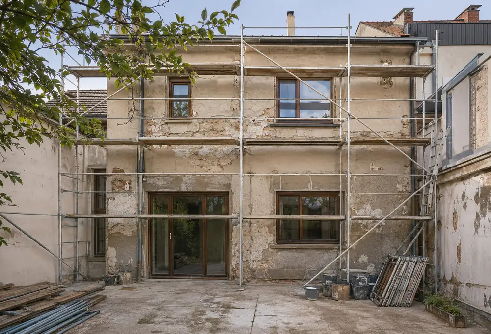 The elevation before the works: failed render stripped back to bare substrate, with scaffold and materials in place